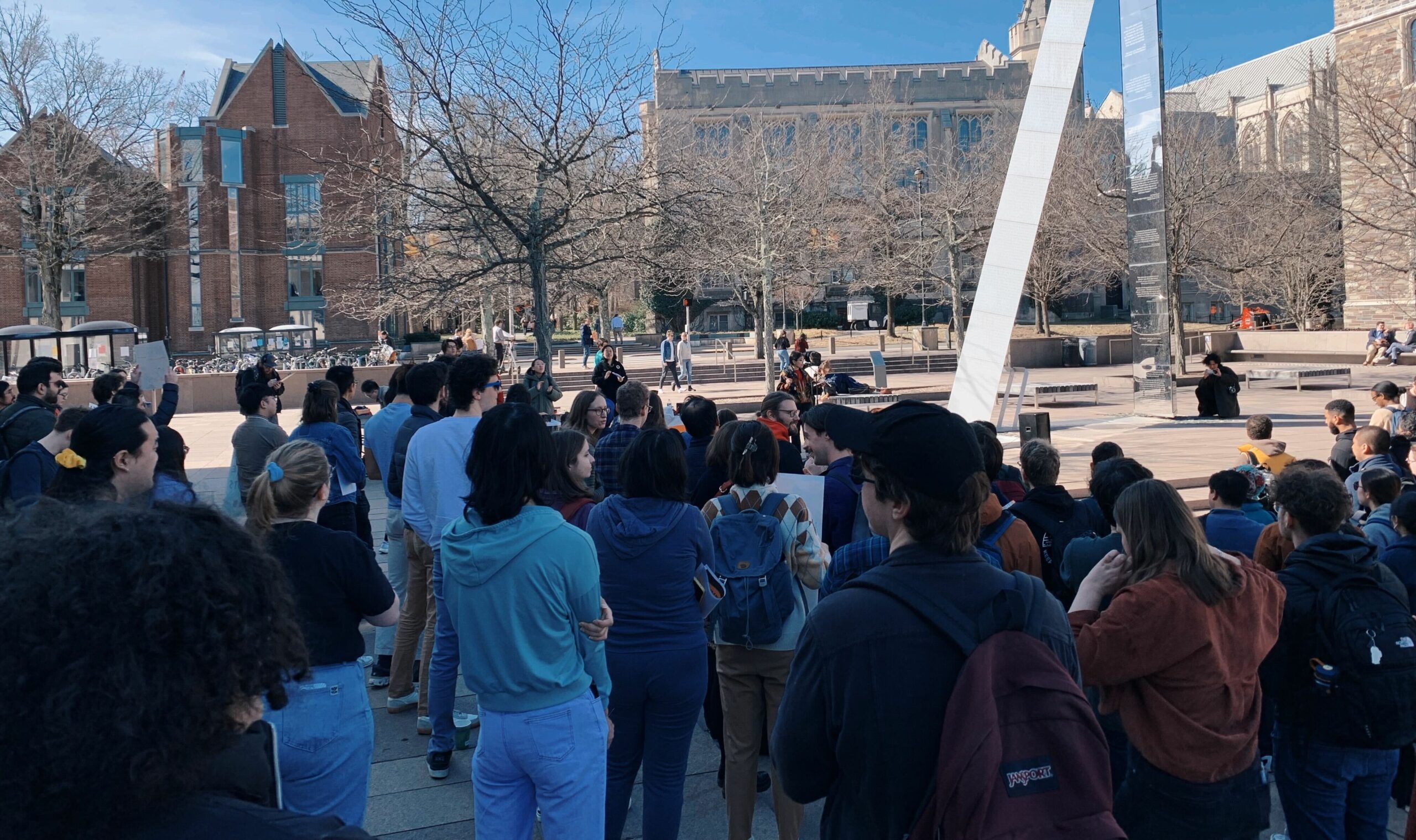 Une photo d'un grand groupe de personnes rassemblées dans une cour du campus de l'Université de Princeton.  Certains tiennent des pancartes mais le spectateur ne peut pas lire ce qui est écrit dessus car les gens font face à la direction opposée à la caméra.  Les arbres sont stériles, marquant les mois d'hiver.