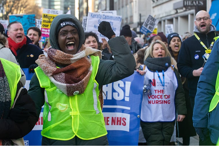 Une femme noire avec le poing levé mène les infirmières en marche illustrant un article sur l'accord de rémunération du NHS