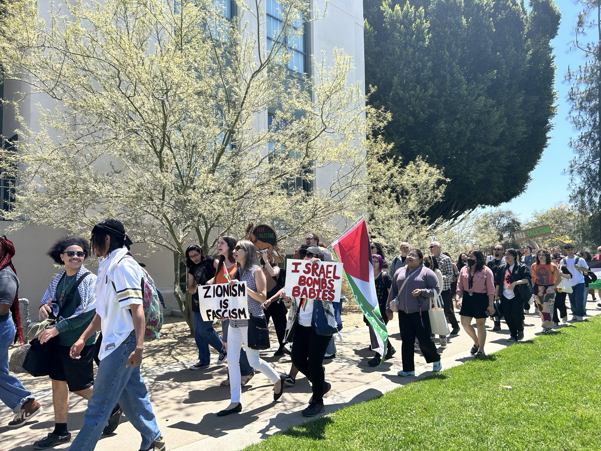 Un groupe de personnes défile en portant un drapeau palestinien et des pancartes indiquant que le sionisme est du fascisme et qu'Israël bombarde des bébés.
